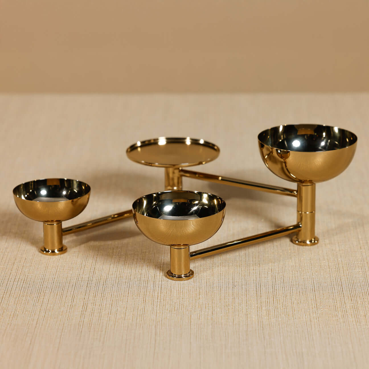 Gold metal three-tiered serving dish on a beige surface
