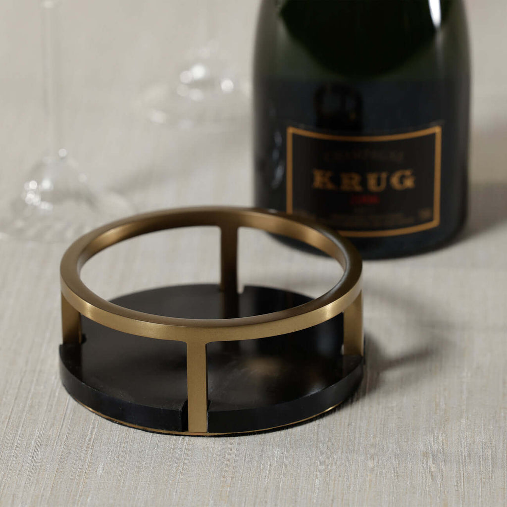 Mirabelle Marble Wine Coaster featuring a black marble base and a brushed brass ring with a bottle of champagne.