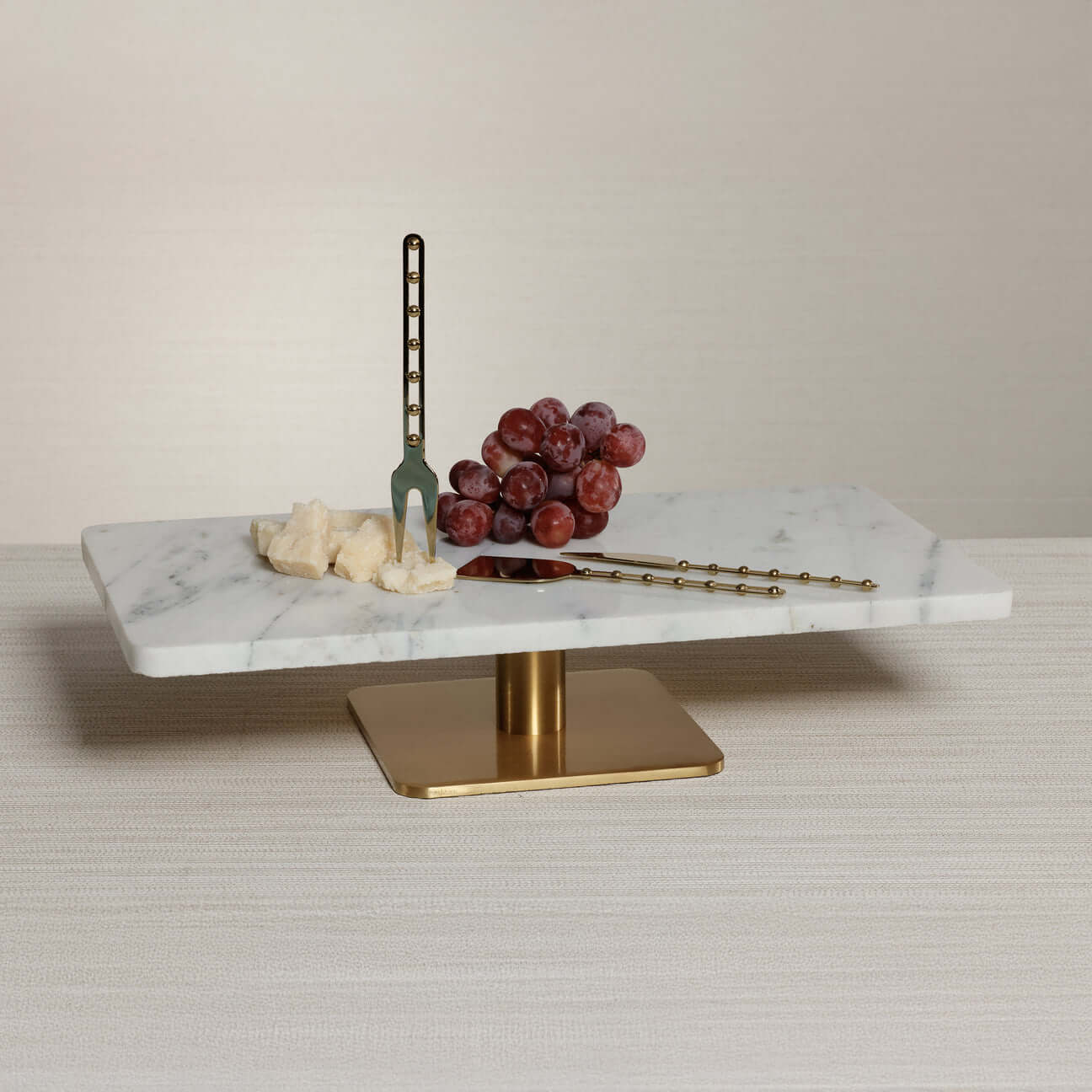 Bodega Cheese and Charcuterie Marble Serving Tray with cheese, grapes, and gold utensils on a table.