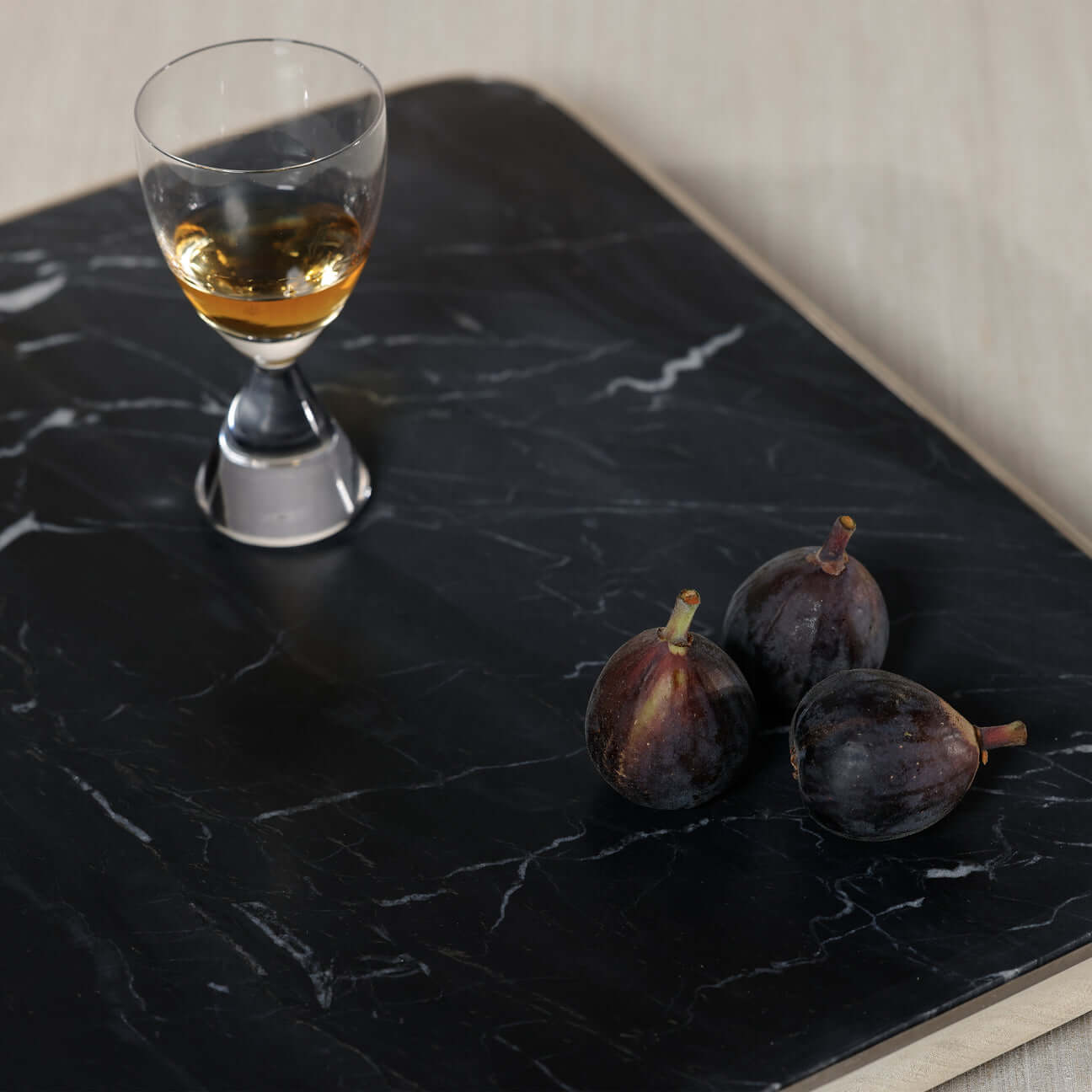 London Cheese and Charcuterie Marble Serving Tray with a glass and figs on a polished black surface.