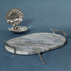 Luze Oval Marble Tray with stainless steel handles and serving utensils on a blue background.