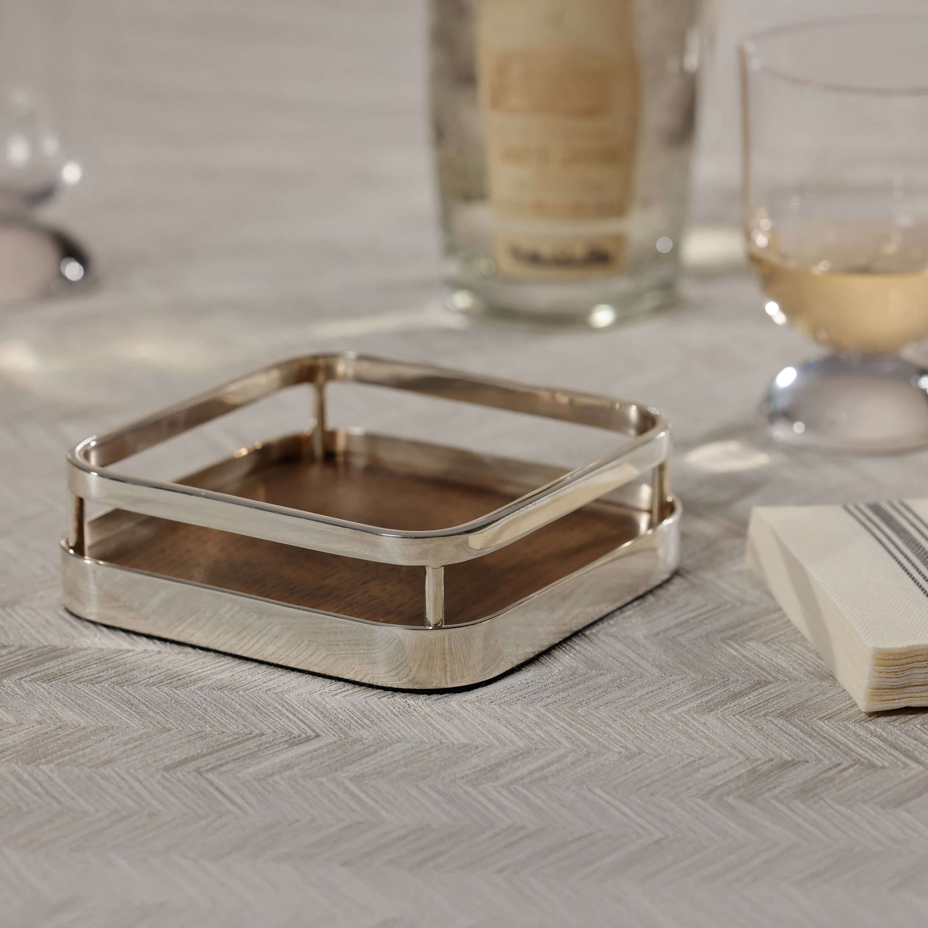 Linea Cocktail Napkin Holder featuring a walnut wood insert and polished nickel frame on a table setting.