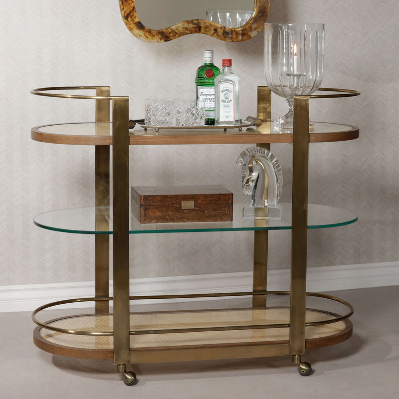 Sloane Oak Wood Oval Bar Cart featuring antique brass frame and glass shelves, perfect for stylish entertaining.