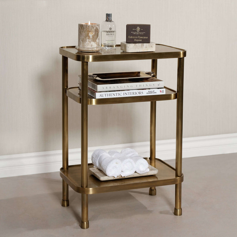 Aman Étagère three-tier open shelving table in antique brass with towels and decor.