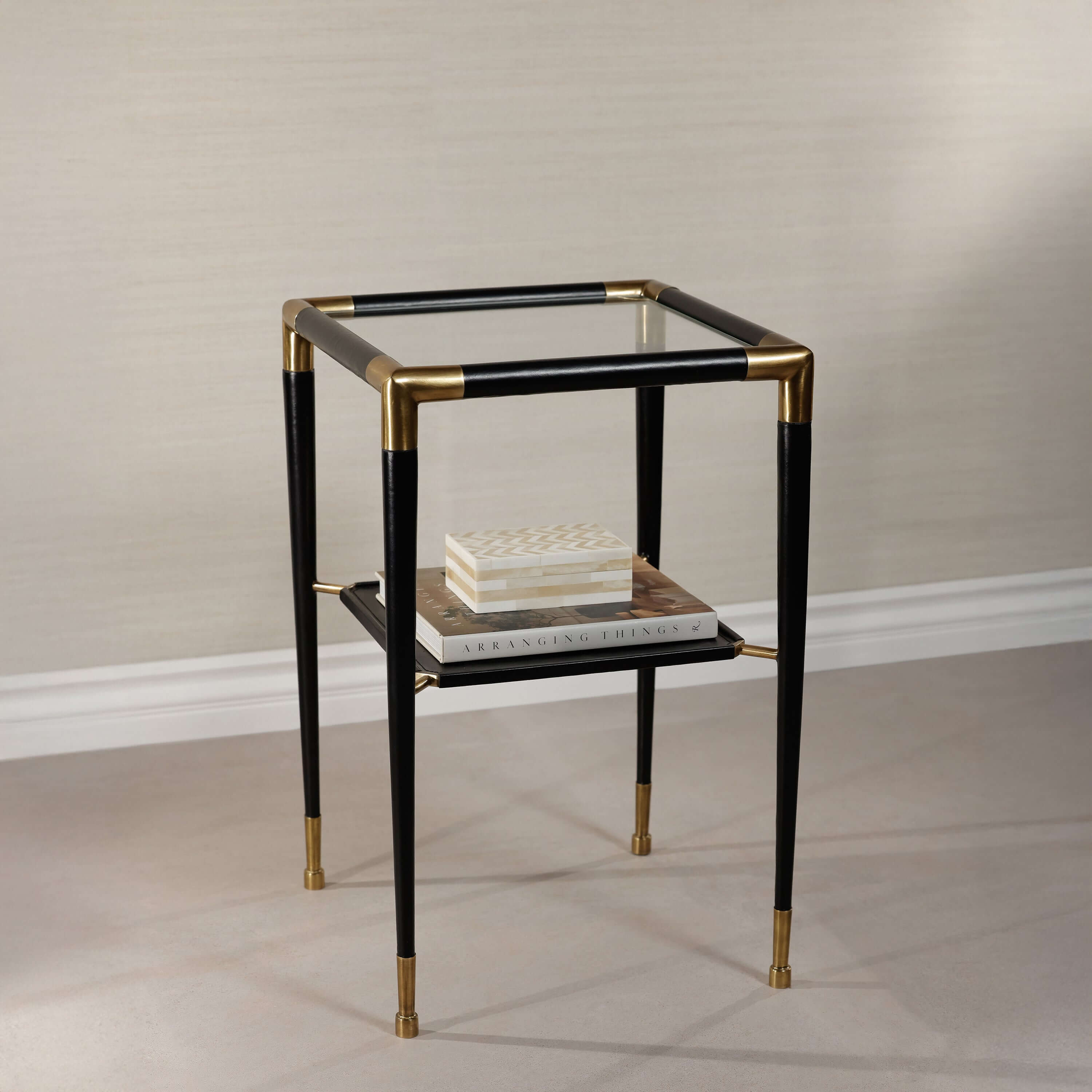 Peninsula Leather Side Table with black leather and brass details, featuring two tiers and a glass top.