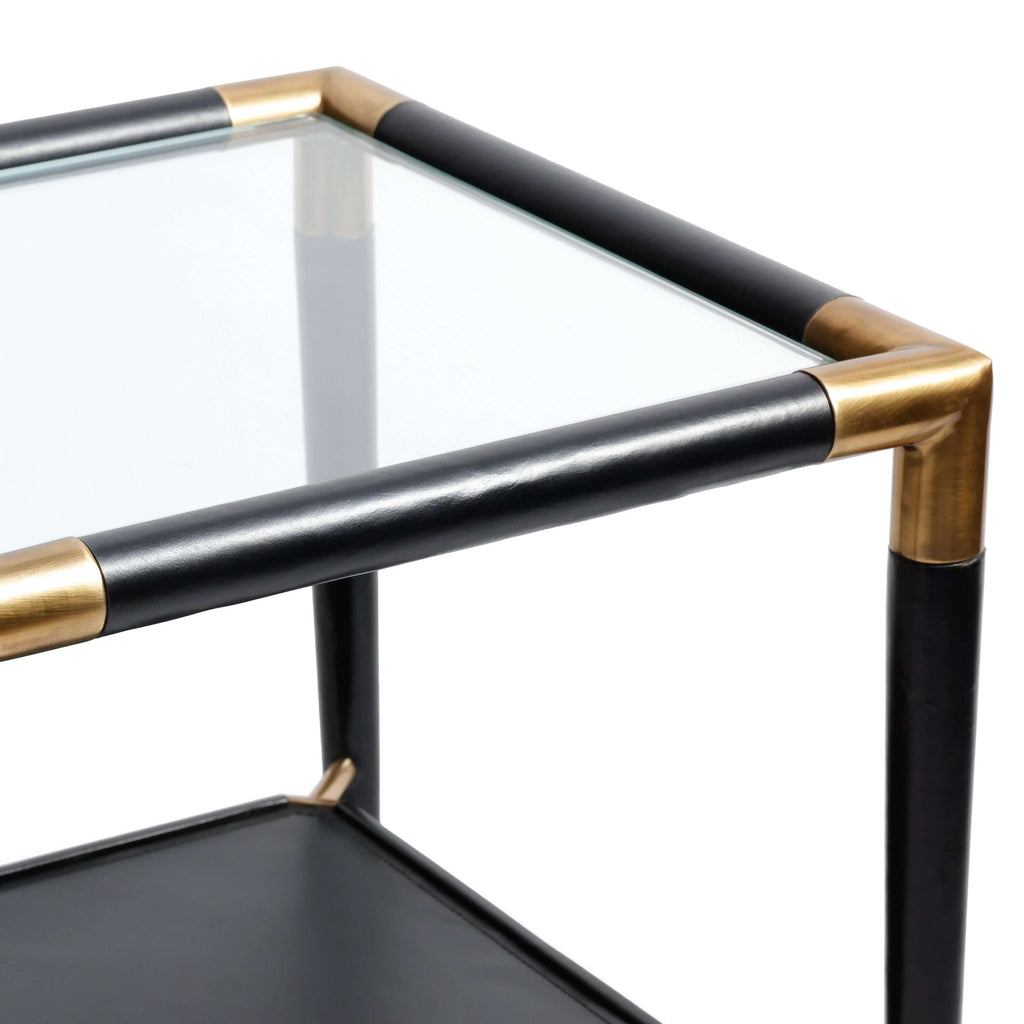 Close-up view of Peninsula Leather Side Table featuring glass top and brass corner joints against a white background.