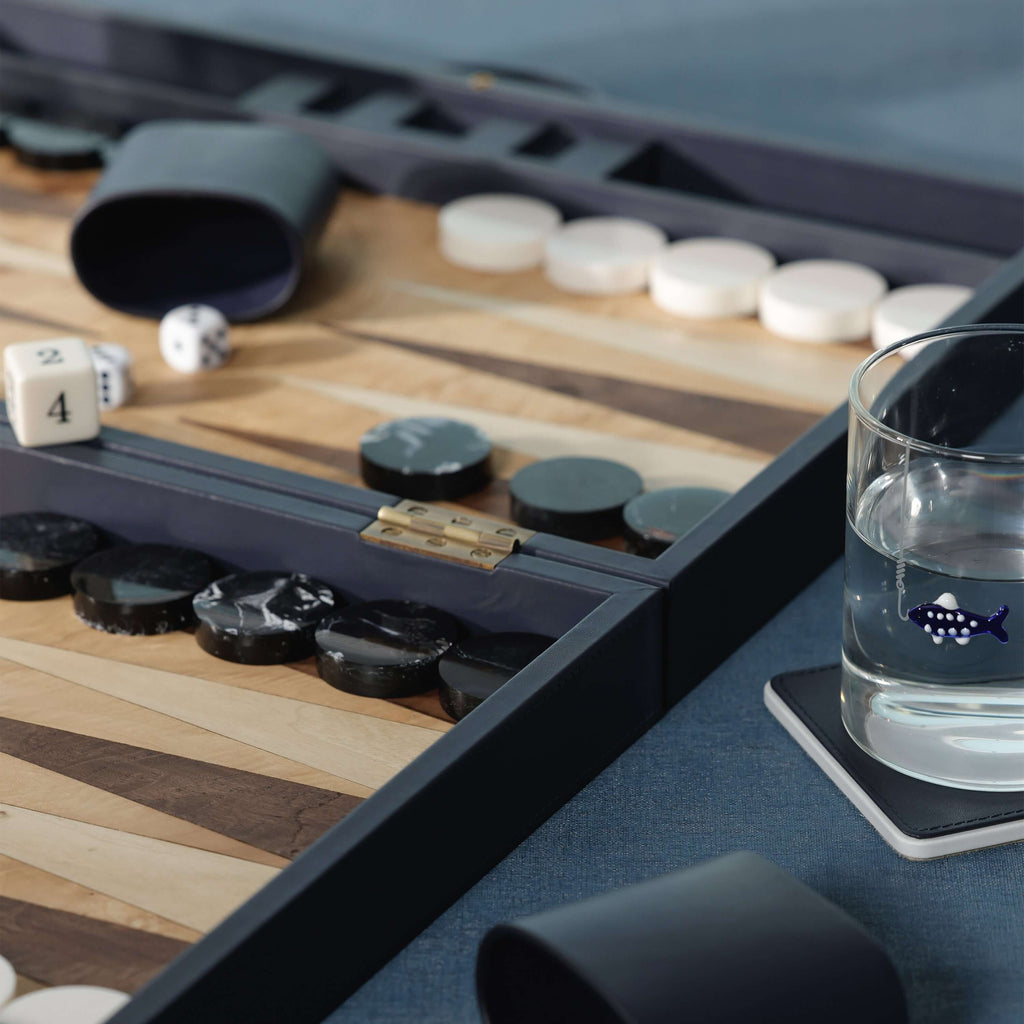 Geneva 19" Backgammon Set - Marine Blue Leather game pieces and cup on a wooden board with a glass of water.