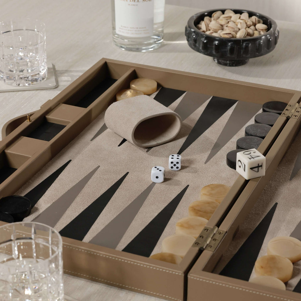 Geneva 19" Backgammon Set - Taupe Leather with dice on a smooth playing surface and elegant drinkware in the background.