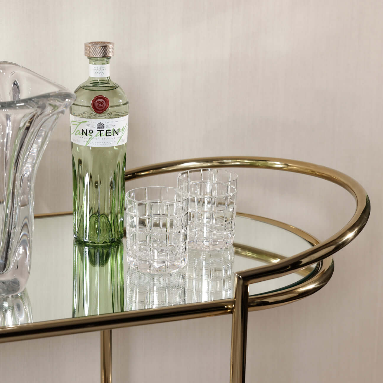 Lido Console Bar Cart featuring a green bottle and crystal glasses on a reflective surface.