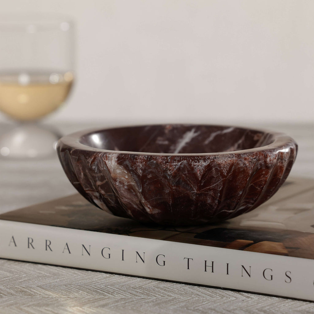 Selene Marble Bowl displayed on a book with a glass in the background, showcasing elegant marble craftsmanship.