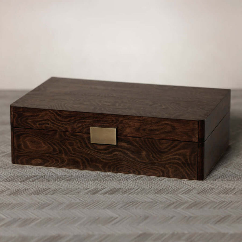 Linea Madrona Burl Veneer Jewelry Box in rich lacquered wood with brass clasp on a textured surface.
