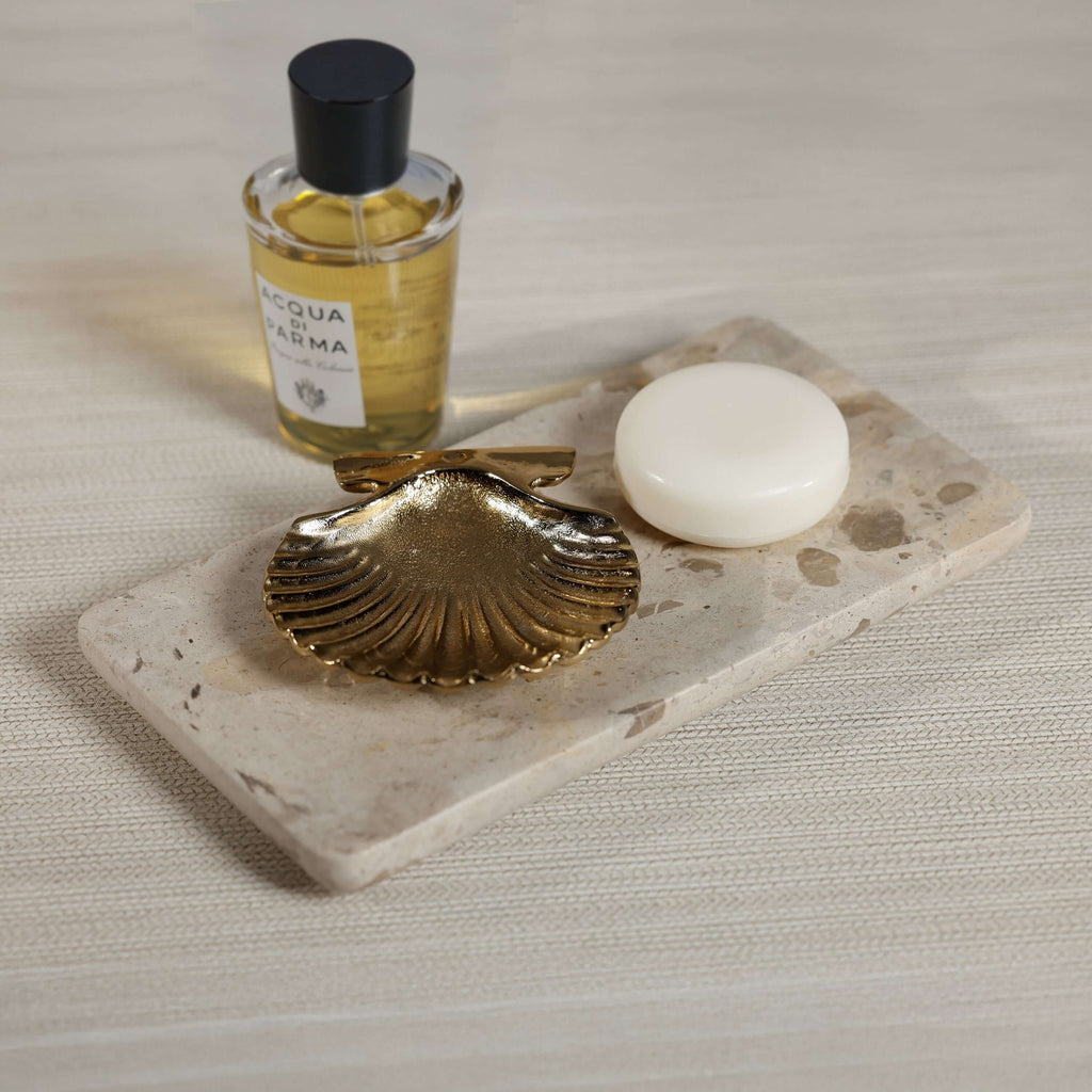Crema Fossil Marble Bath Collection displayed with gold shell dish, soap, and fragrance bottle on a marble tray.
