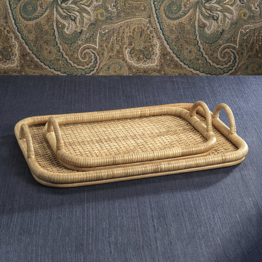 Tropique Rectangular Rattan Trays in small and large sizes, handwoven with natural rattan and wrapped handles, stacked on a dark fabric surface.