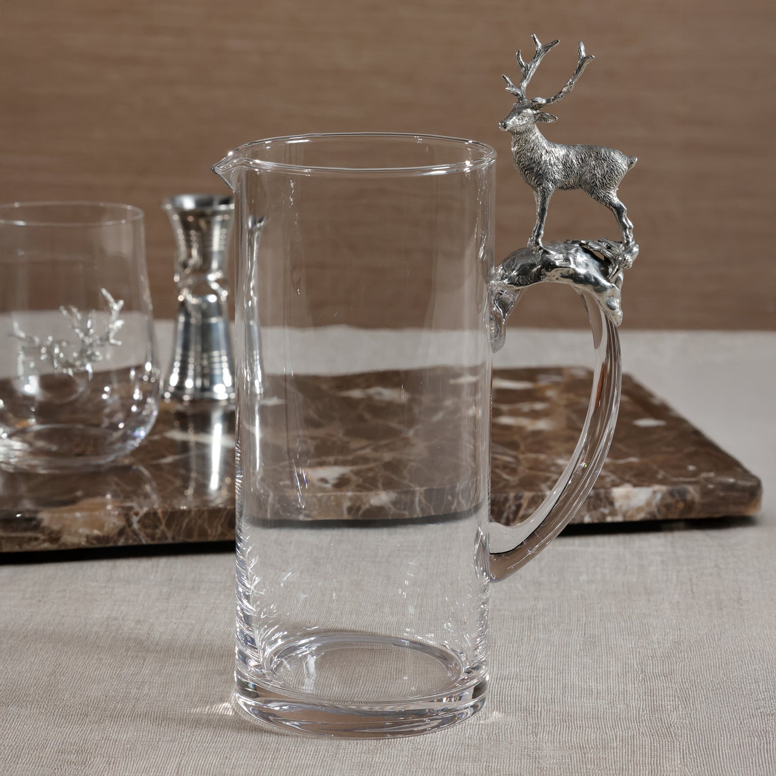 Clear glass pitcher with deer handle on a marble surface