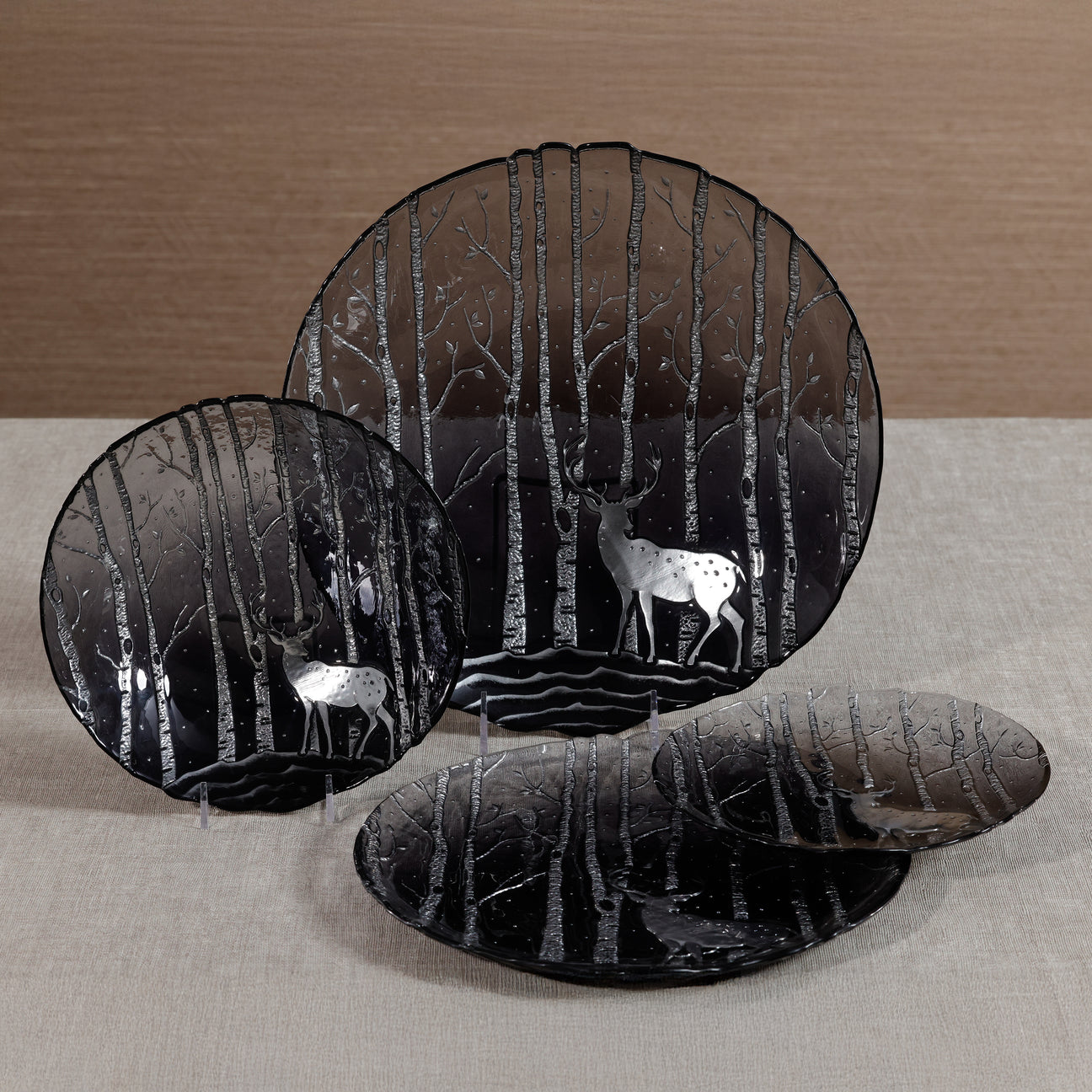 Set of black glass plates with deer and forest design on a neutral background