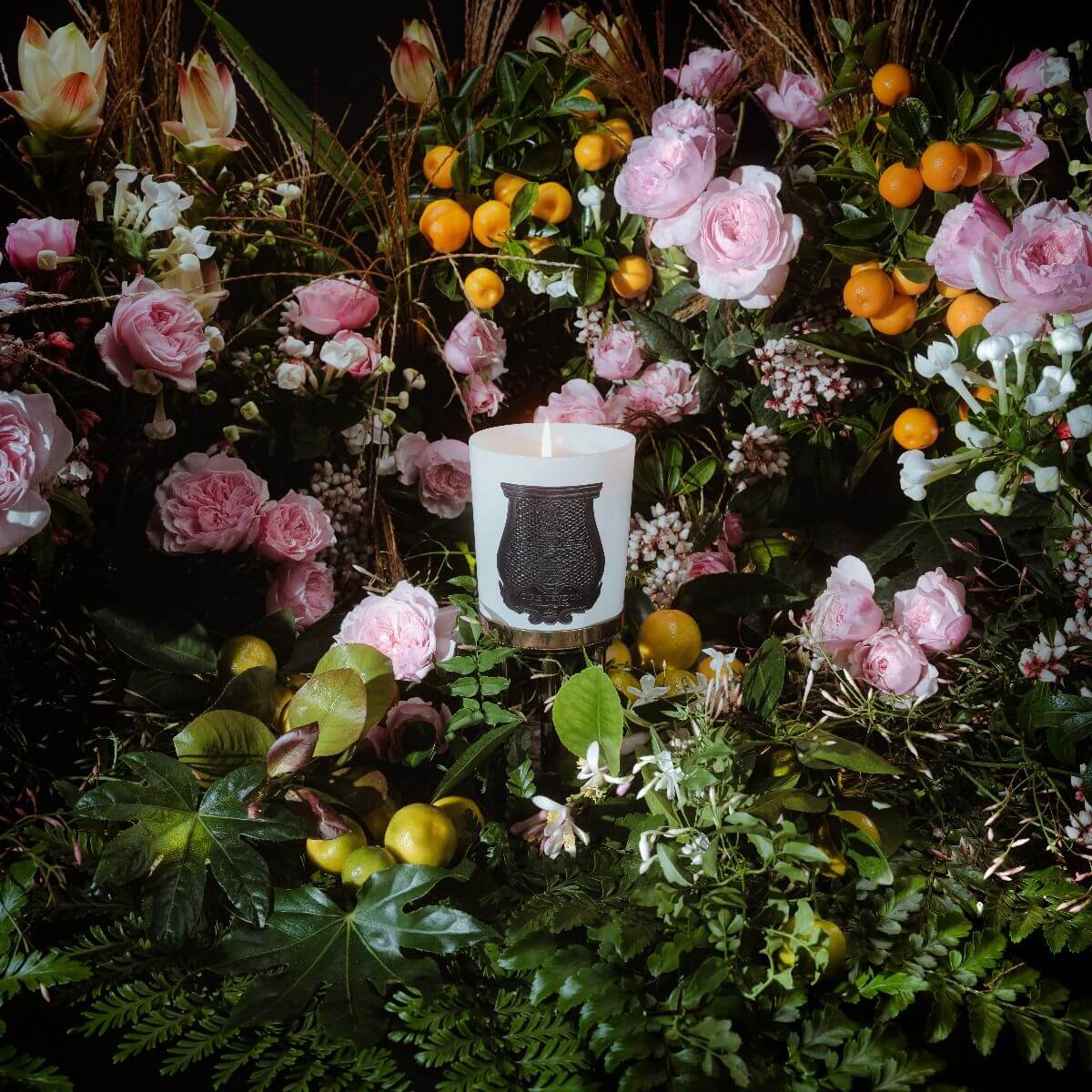 Rose Poivre Classic Candle surrounded by lush pink roses and greenery, showcasing elegant floral decor.