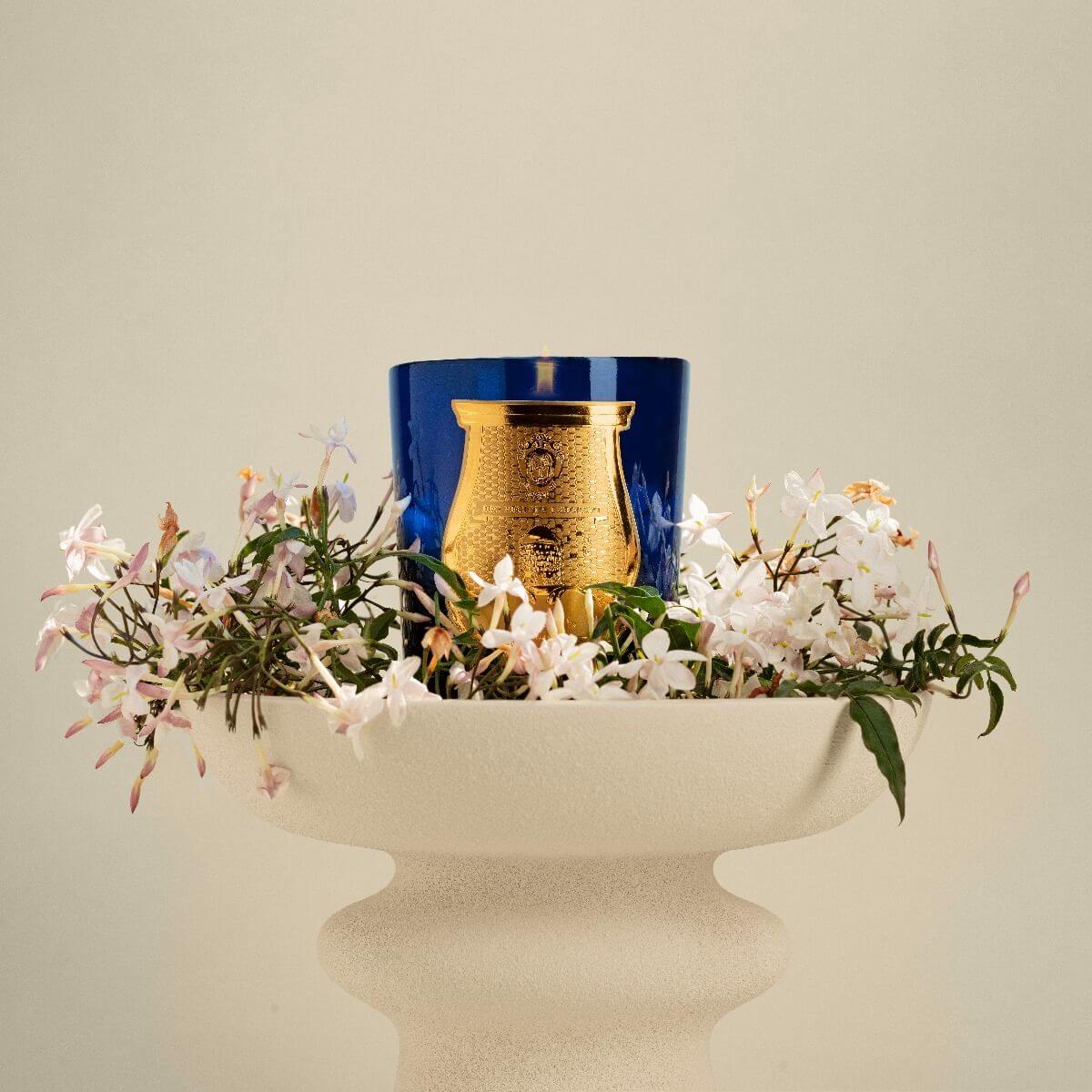 Madurai Classic Candle displayed in a blue holder surrounded by delicate white flowers.